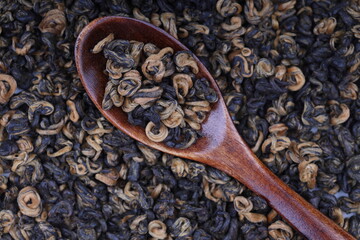 Red twisted tea leaves in a wooden spoon. Chinese black tea is scattered on the table in large quantities. Golden spirals. view from above.