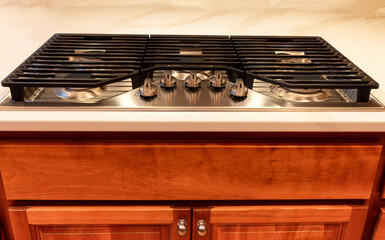 Fototapeta premium Modern natural gas Kitchen stove top cook surrounded by stone countertop and cherry wood cabinets