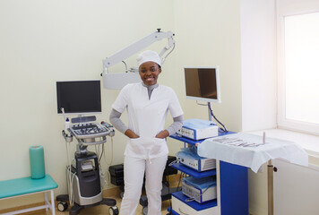 An African-American female doctor in a white coat stands in the treatment room. © Tatsiana
