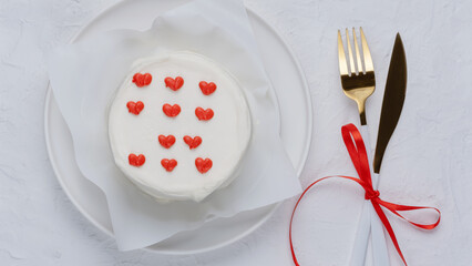 White cake with hearts on a white plate with a knife and fork