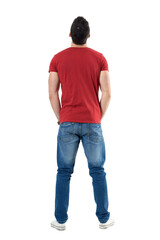 Back view of young casual man with hands in pockets looking up. Full body length portrait isolated...