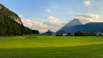 Beautiful mountain scenery near Kufstein, Austria showing fresh green fields and the Kufstein castle on a hill in the background.