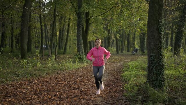 Woman with earphones running through an autumn forest at sunset in slow-motion