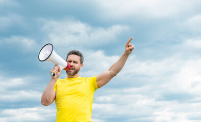 man in yellow shirt shout in megaphone on sky background with copy space