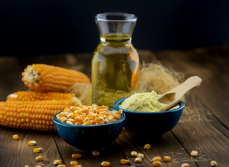 Close-up of dry corn cob, cornmeal, corn oil on rustic wooden table.
