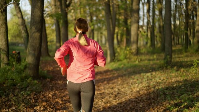 Young blonde girl wearing pink tracksuit and leggings running in the autumn forest at sunset. Slow-motion