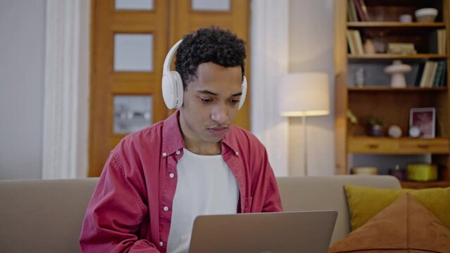 Slow motion, young handsome multi-ethnic guy putting on wireless headphones, telecommuting on laptop