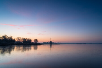 Fototapeta na wymiar Colourful dawn over a frozen lake with a windmill.