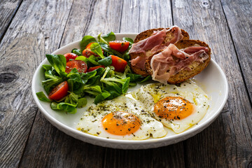 Breakfast - sunny side up egg, toasted bread with ripening ham and vegetables served on wooden table
