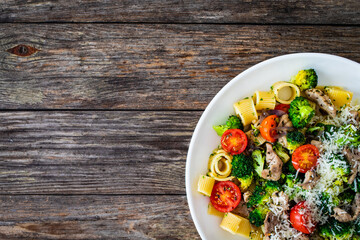 Pasta with roasted pork loin, broccoli, parmesan and cherry tomatoes on wooden table