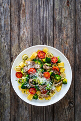Pasta with roasted pork loin, broccoli, parmesan and cherry tomatoes on wooden table