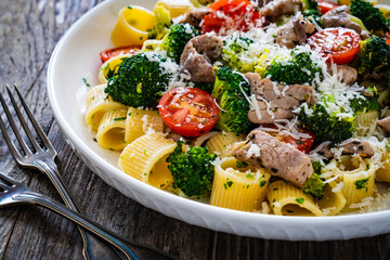 Pasta with roasted pork loin, broccoli, parmesan and cherry tomatoes on wooden table