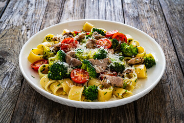 Pasta with roasted pork loin, broccoli, parmesan and cherry tomatoes on wooden table