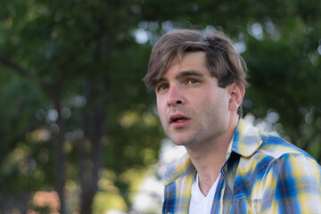 A young white man outdoors in a shady backyard setting with a serious expression.