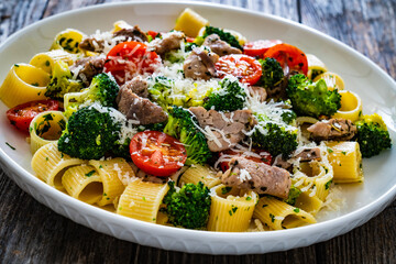 Pasta with roasted pork loin, broccoli, parmesan and cherry tomatoes on wooden table