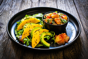 Salmon ceviche with lemon, mango and avocado on wooden table
