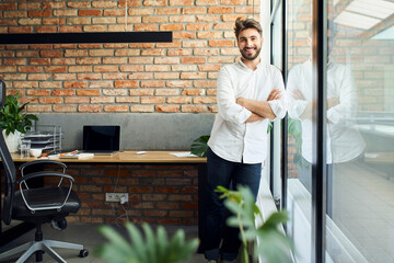 Successful casual businessman standing in modern office leaning against window