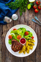 Fried beef sirloin with potatoes and vegetables on wooden table
