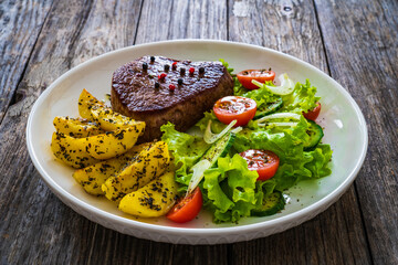 Fried beef sirloin with potatoes and vegetables on wooden table
