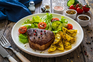 Fried beef sirloin with potatoes and vegetables on wooden table
