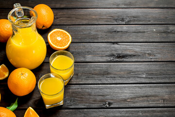 Orange juice in pitcher with fresh oranges.