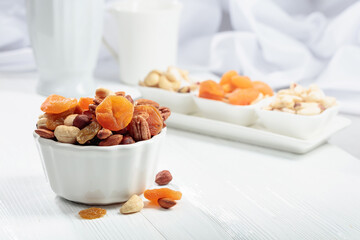 Dried fruits and assorted nuts on a white table. - obrazy, fototapety, plakaty
