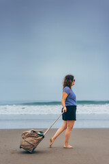 vertical image of a girl walking on the sand with a travel bag.copy space
