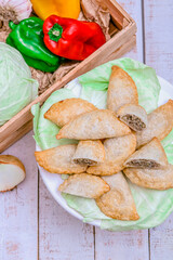 Meat and cabbage empanadas. White wooden background. Ingredient around. Zenithal.