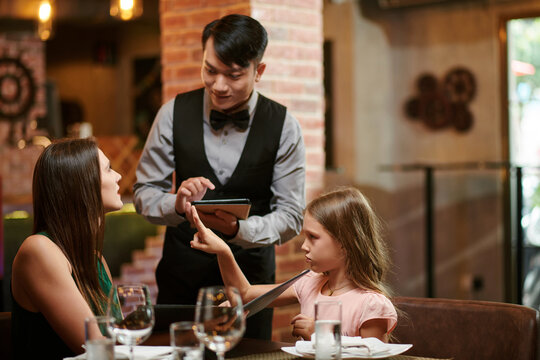 Fancy restaurant waiter taking order from mother and daughter