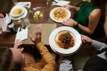 Waiter serving plate of spaghetti bolognese for man, view from above
