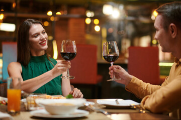Happy couple toasting with glasses of red wine when sitting at dinner table