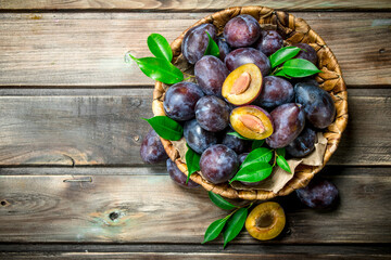 Halves and whole plums with leaves in the basket.