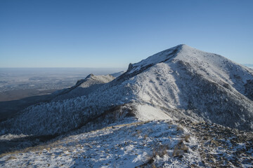 Winter snowy panorama of neighboring mountains and hills from Mount Beshtau with snow-covered and icy grass, sunny winter day