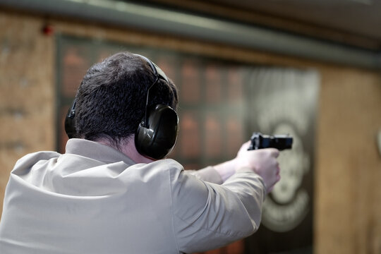 A man shoots a pistol in a shooting range, rear view.