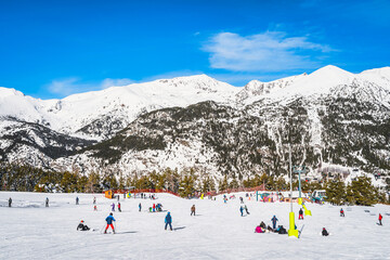 People, families and kids having fun and learning how to ski and snowboard on El Tarter green...