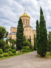 Fototapeta na wymiar Tsminda Sameba or Holy Trinity Cathedral of Tbilisi, Georgia. Modern religious complex of Georgian Orthodox church with with golden dome surrounded by cypress trees in neat garden