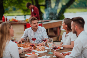 Group of happy friends having picnic french dinner party outdoor during summer holiday vacation near the river at beautiful nature