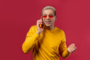 Stylish man talking by phone, nice joke, smiling. Young guy on red background. Having smartphone call.
