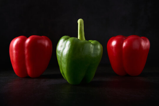 A green pepper in the foreground and two red parika in the background. Foreground and background are in black pattern. Also suitable for mature vs immature concepts.