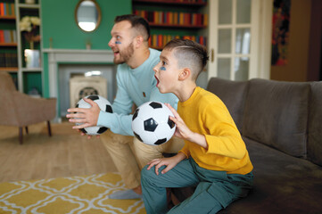 Excited father and son cheering and watching football match at home