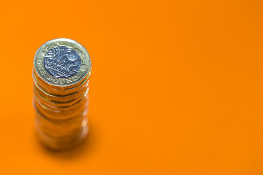 One Stack Of Uk Sterling Gold Coloured Pound Coins. Photographed From Above On A Bright Orange Background With Copy Space.