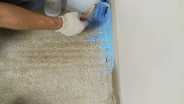 Sticking damper tape and applying waterproofing. The process of priming the floor with white paint. The master applies white waterproofing to the floor. The master applied waterproofing and damper tap