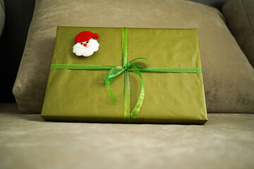 Gift box with green bow and Santa Claus head lying on sofa, close-up
