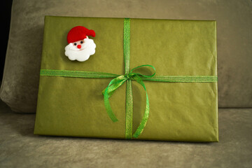 Gift box with green bow and Santa Claus head lying on sofa, close-up
