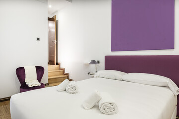 Obraz na płótnie Canvas Bedroom with a double bed with a white feather duvet with white shelves as bedside tables with twin lamps and a fuchsia upholstered headboard and matching barefoot chair