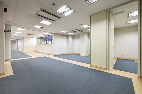 Rooms of an empty office with one with windows, technical ceilings, blue carpeted floors and individual offices