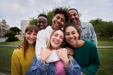 Young people embrace posing for a group portrait looking at the camera outside. Smiling friends of the millennial generation. Young guys and girls having fun together