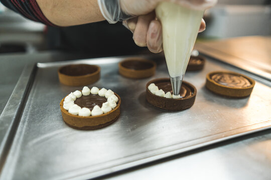 baker piping cream on chocolate cakes at the bakery, dessert concept. High quality photo