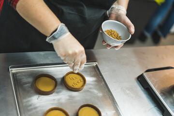 top view of chef's hands adding golden sprinkles to round cakes in the bakery. High quality photo