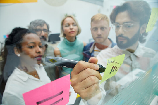 Creative Colleagues Meeting In Office. Diverse Business People Team Workers Standing In Brainstorming, Discussing New Ideas For The Future Of The Company, Writing On Paper Note. 